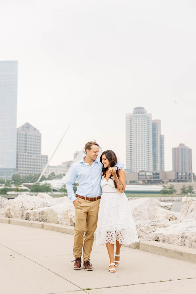 Couple walking on a path with the Milwaukee Skyline in a the background. 
