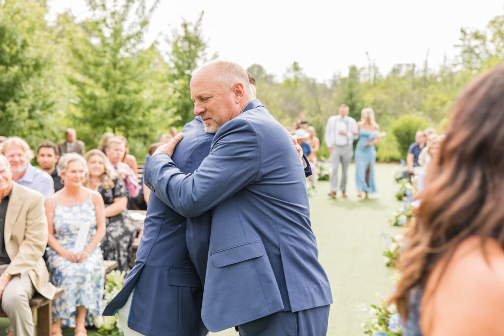 Father of the groom hugging groom in the aisle. 