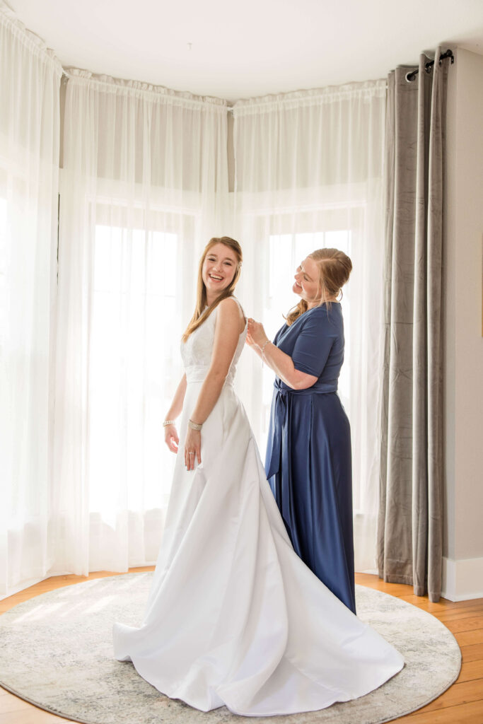 Mother helps bride with the buttons on her wedding dress at the Bowery in Lake country, Wisconsin.