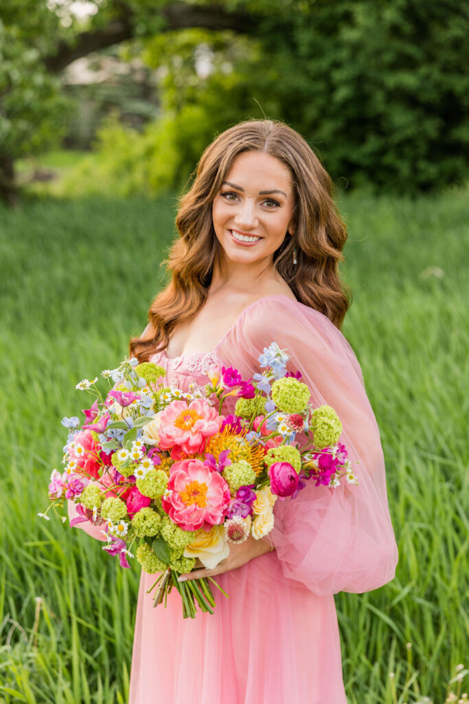 Bride smiling at the photographer in a pink ball gown florals designed by Flora Elements.