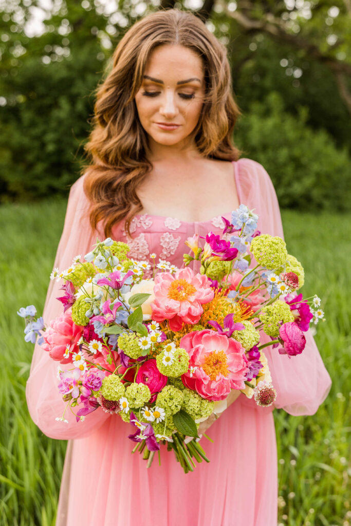 Bride in pink wedding dress looking down at her bridal bouquet designed by Flora Elements. 