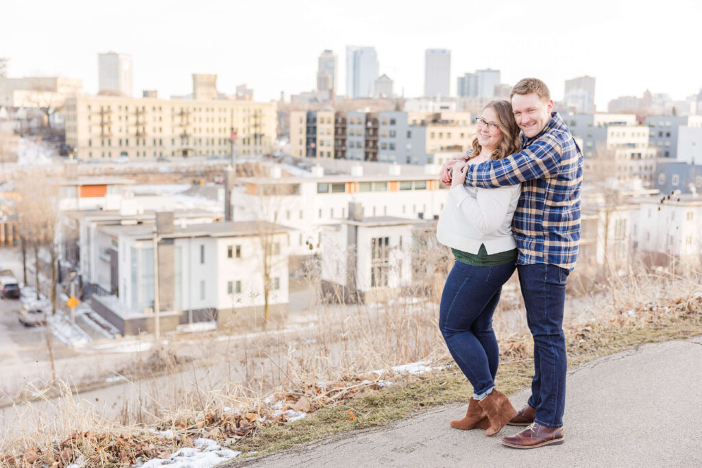 Engaged couple smiling with the Milwaukee Wisconsin skyline in the background.