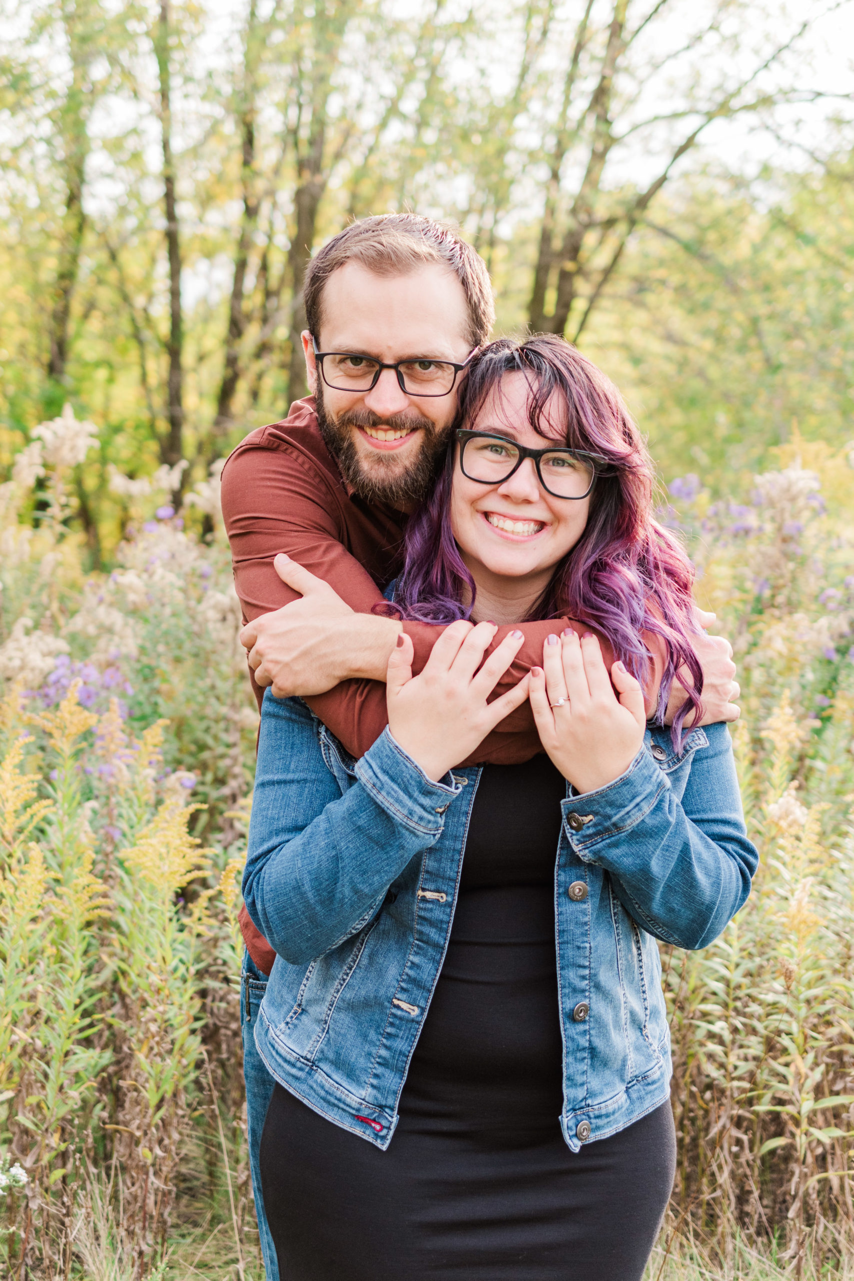 couple looking directly at the camera and smiling with fall flowers and leaves in the background
