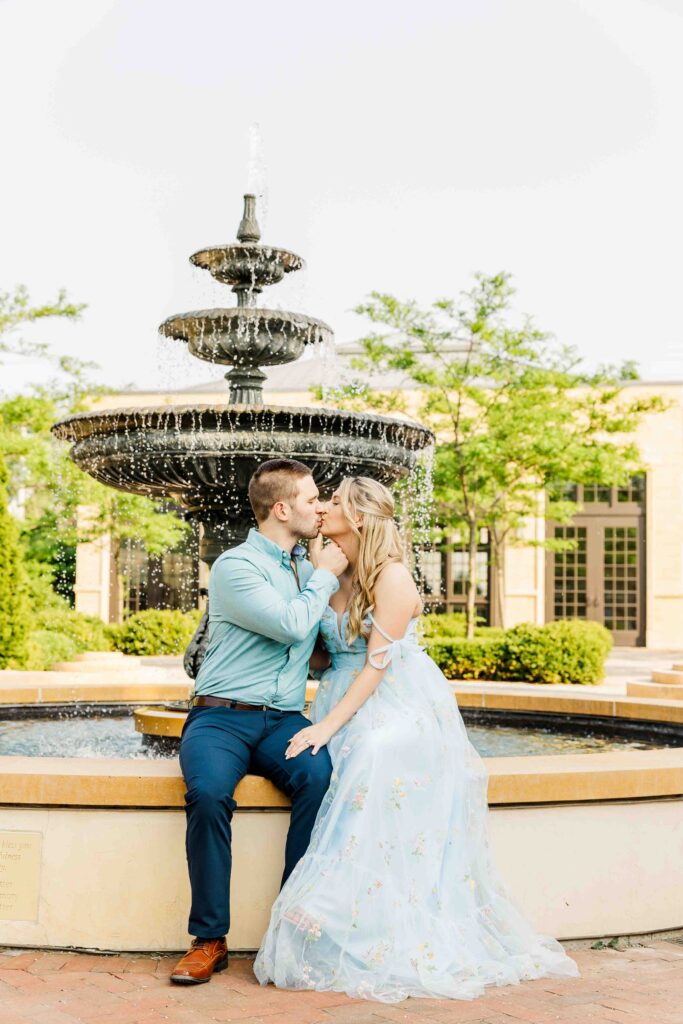 Couple kisses in front of water fountain. 