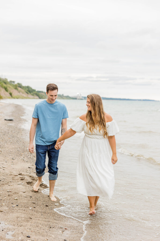 Engaged couple laughing, walking on a beach during their engagement session in Wisconsin on Lake Michigan. 