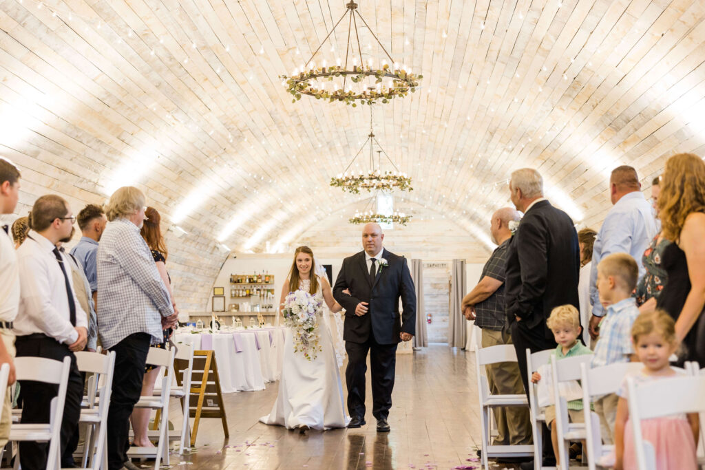 Bride being walked down the aisle by her father in in the Bowery barn in Wisconsin.