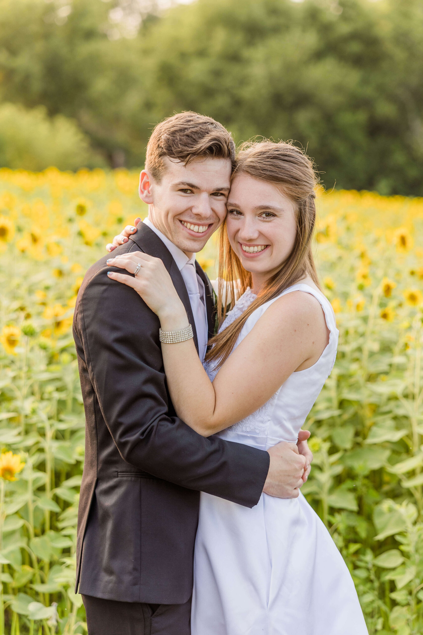 Bride and groom looking at camera during golden hour portraits in a sunflower field on their wedding day.