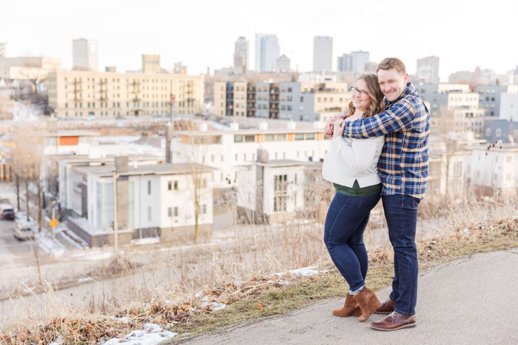Engaged couple smiling with the Milwaukee Wisconsin skyline in the background. 