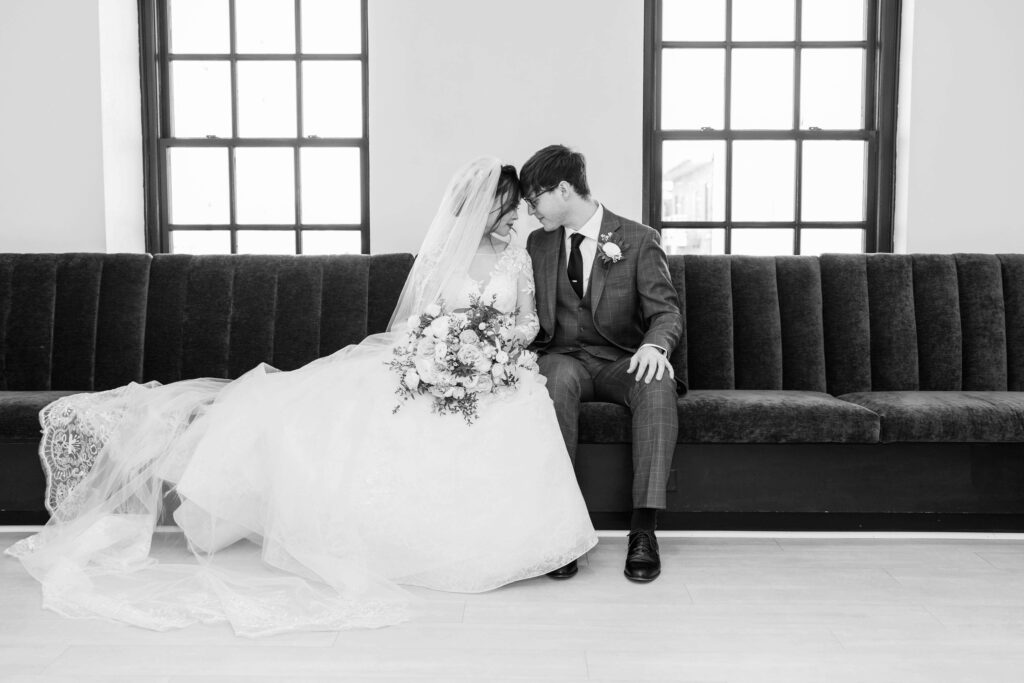 Couple resting foreheads together on velvet couch in black and white on their wedding day in 10 South outside of Madison, Wisconsin. 